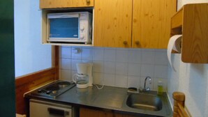 Una cocina compacta con armarios de madera, un microondas, una cafetera y un lavabo.