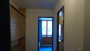 Un pasillo estrecho con paneles de madera en un lado y una alfombra azul. Una puerta da a un balcón con vistas a árboles.