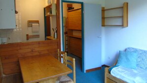 Una habitación acogedora con una mesa de madera y sillas, un pequeño sofá y un estante empotrado con varios objetos.