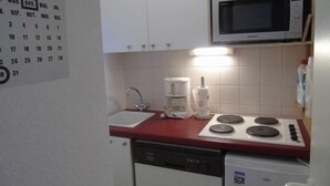 Kompakti keittiö, jossa on valkoiset kaapit, mikroaaltouuni, kahvinkeitin ja astianpesukone.