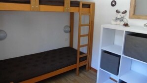 Kerrossänky, jossa on tikkaat, valkoinen hyllykkö ja hyllyllä pehmolelu.