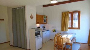 A compact kitchen with a microwave, oven, and sink. There's a dining table with chairs, a bed with a window, and a curtain. - Cozy apartment, pets welcome - 6 guests (Valfréjus)