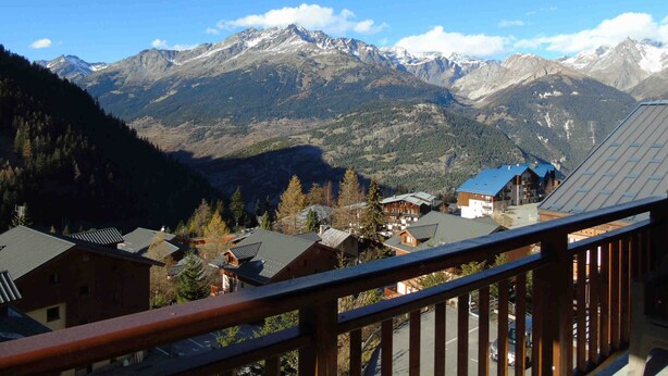 A mountain resort with chalet-style buildings, a wooden balcony, and a view of snow-capped peaks. - Cozy apartment, pets welcome - 6 guests (Valfréjus)