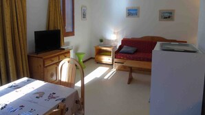 A cozy living room with a television, a red sofa, a wooden table, and a green chair. - Cozy apartment, pets welcome - 6 guests (Valfréjus)