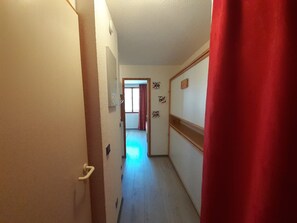 A narrow hallway with a door on the left, a red curtain on the right, and a window at the end.