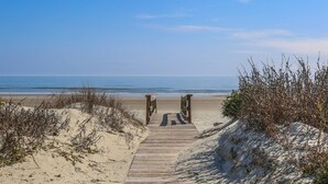 A wooden boardwalk leading to a beach with sand dunes and sparse vegetation.