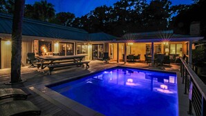 A swimming pool with a wooden deck, outdoor seating, and a covered patio area.