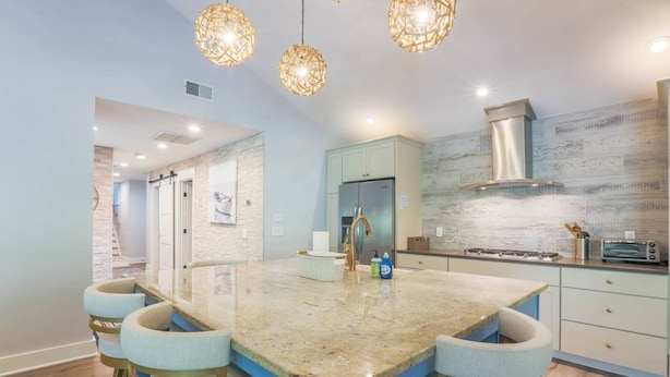 A modern kitchen with a central island, bar stools, a stainless steel refrigerator, and a gas stove.