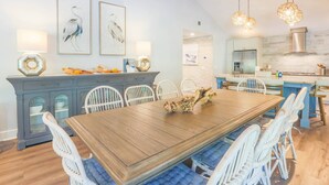 A dining area with a wooden table and white chairs, a kitchen with a stove and refrigerator, and wall-mounted artwork.