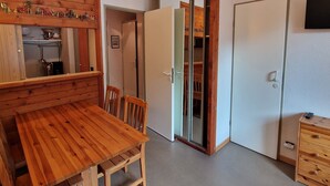 Ein kompakter Raum mit Esstisch und Stühlen aus Holz, einer Schiebetür zu einem Kleiderschrank und einer kleinen Holzkabine mit Schubladen.