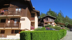 A chalet-style building with balconies, a sign reading "les bruyères," and a parking area with cars.
