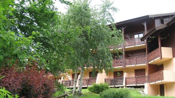 A multi-story building with balconies, surrounded by greenery and a small garden area.