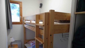Une chambre avec un lit superposé, une fenêtre, une petite table avec une lampe et un radiateur.