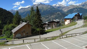 Une station de montagne dotée d’un parking, de bâtiments aux toits bleus et, en arrière-plan, de montagnes enneigées.
