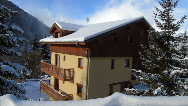Un chalet à deux étages doté d’un balcon, entouré d’arbres et de montagnes couverts de neige.