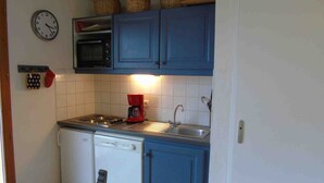 Une cuisine compacte équipée d’une cuisinière, d’un évier et d’un lave-vaisselle, avec des meubles bleus et une horloge au mur.