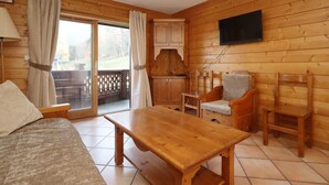 A wooden cabin with a sofa, a wooden table, a TV mounted on the wall, and a sliding glass door leading to an outdoor area. - 2-room apartment, 5 pers., skiing, parking, pool (Les Houches)