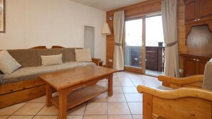 A cozy living room with a wooden sofa, a wooden coffee table, and a wooden armchair. There is a sliding glass door leading to an outdoor area. - 2-room apartment, 5 pers., skiing, parking, pool (Les Houches)