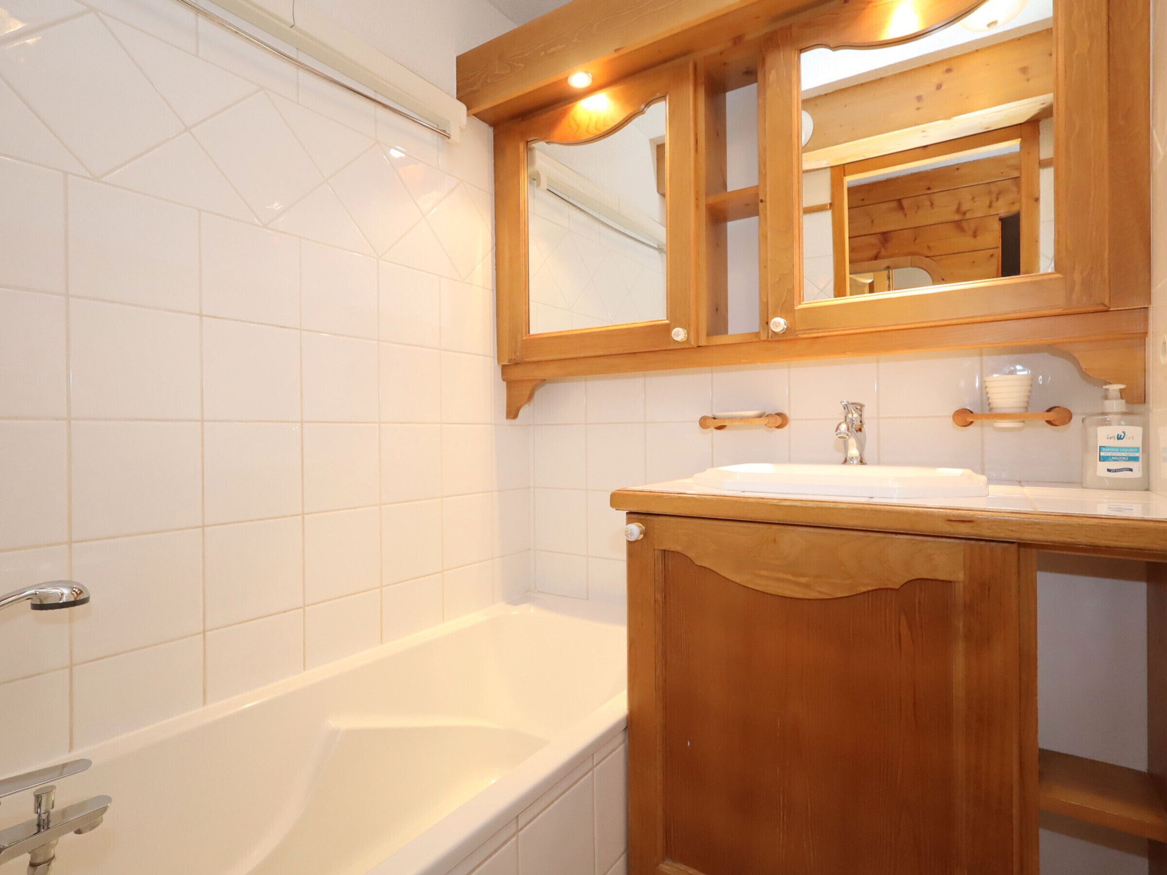 A bathroom with a white bathtub, wooden vanity, and a mirror above the sink.