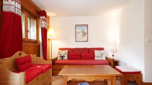 A cozy room with a wooden sofa, a wooden table, and a red patterned sofa.