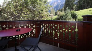 A balcony with a red table and chairs, a decorative metal fence, and a mountainous landscape in the background.