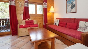 A cozy room with a wooden interior, a red sofa, a wooden table, and a window with curtains.