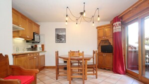 A kitchen with wooden cabinets, a dining table with chairs, a chandelier, and a red curtain.