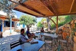 An outdoor seating area with tables and chairs, surrounded by stone walls and greenery. - Apartment- Bilocale - One Bedroom Apartment, Sleeps 2 (Favignana)