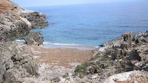Una costa rocosa con una playa y un mar azul cristalino.