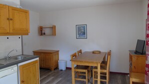 Una cucina compatta con mobili in legno, un lavello, un tavolo da pranzo con sedie, uno sgabello e una mensola con libri.