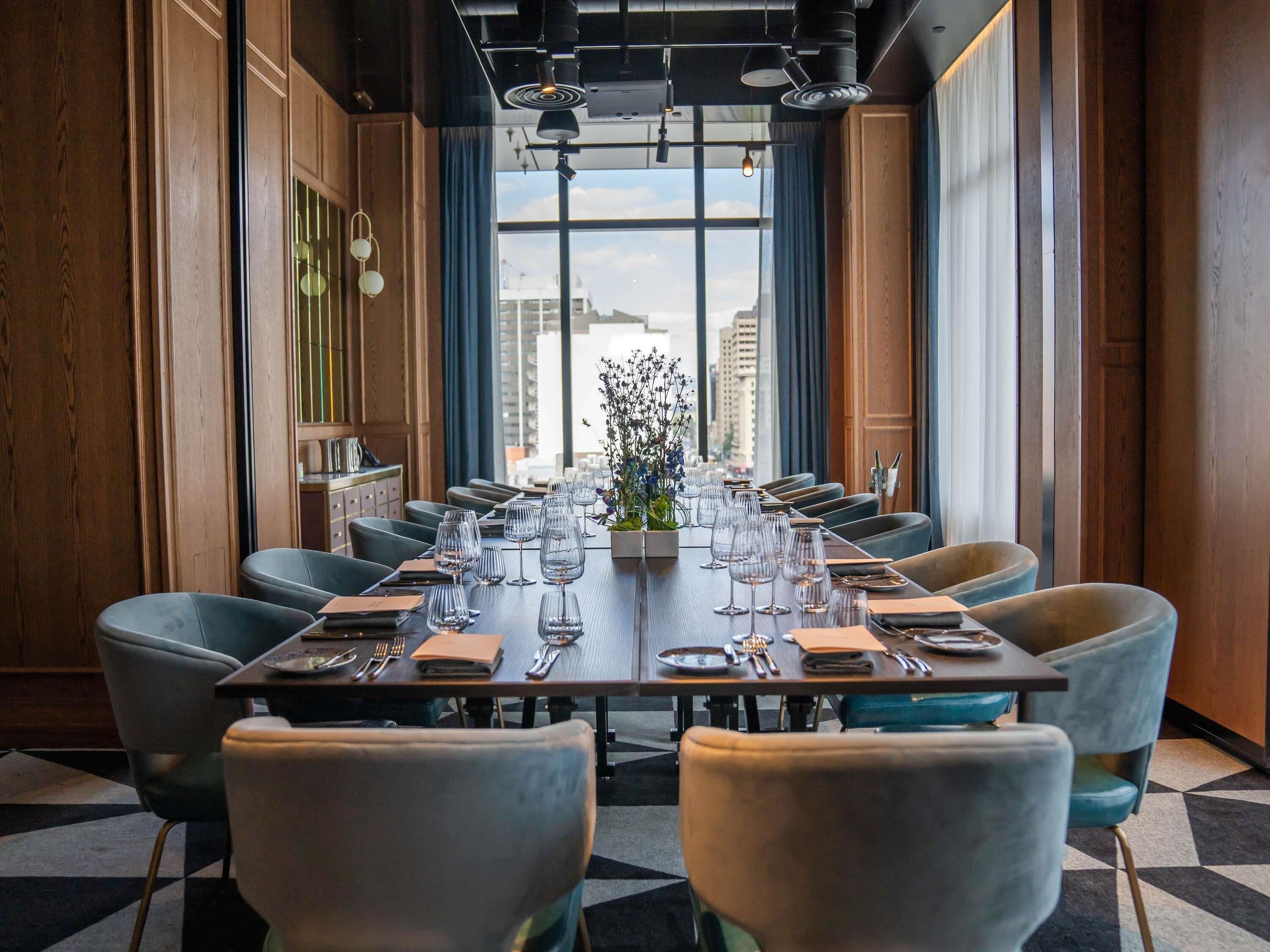 A conference room with a long table, chairs, and a view of the city through large windows.