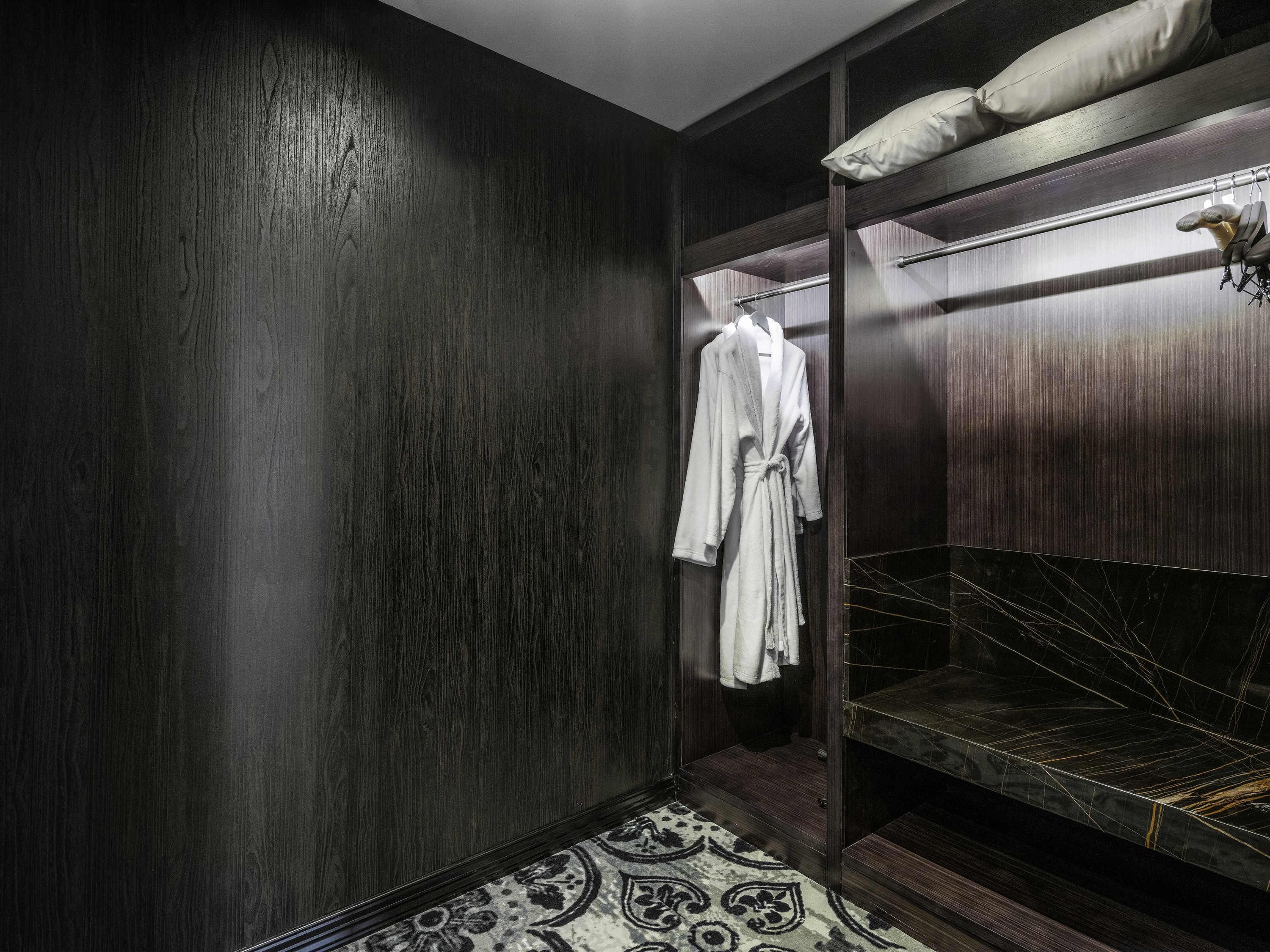 Una habitación con paneles de madera oscura, una cama, una bata colgada y una alfombra estampada.