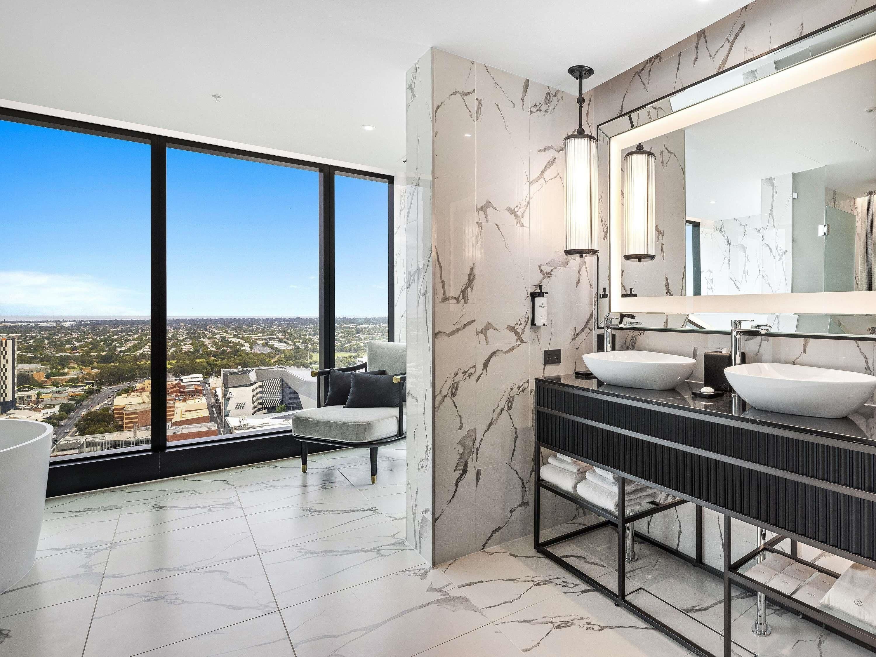 A modern bathroom with a large window, marble walls, and a dual sink vanity.
