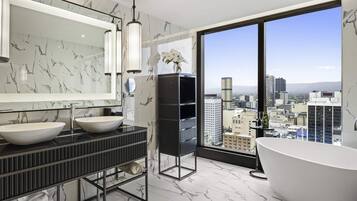 A modern bathroom with two sinks, a large mirror, a freestanding bathtub, and a city view through large windows.