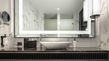 A modern bathroom with a large mirror, marble tiles, a white sink, and a black countertop.