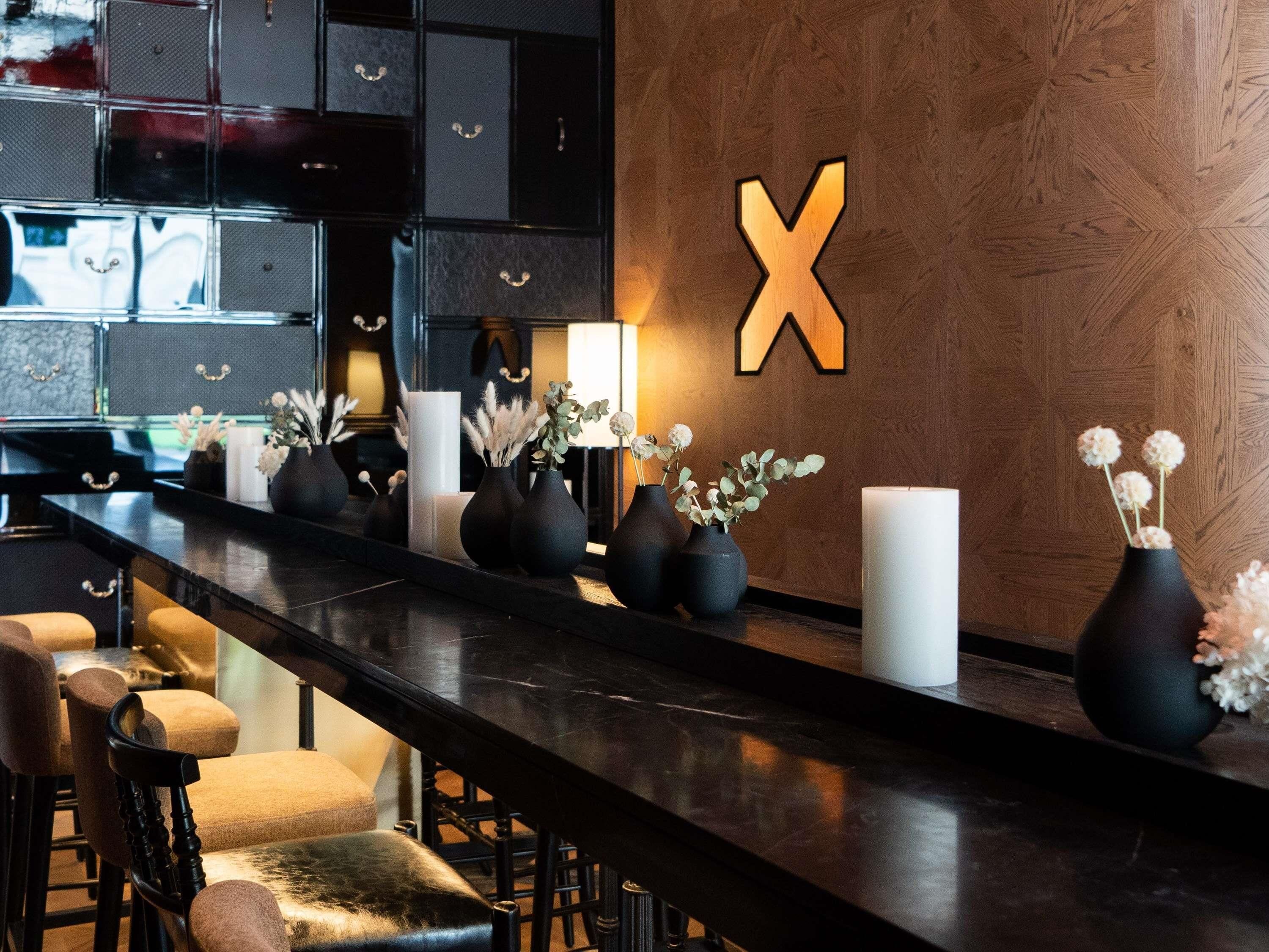 A bar area with a long counter, black bar stools, and vases with flowers.
