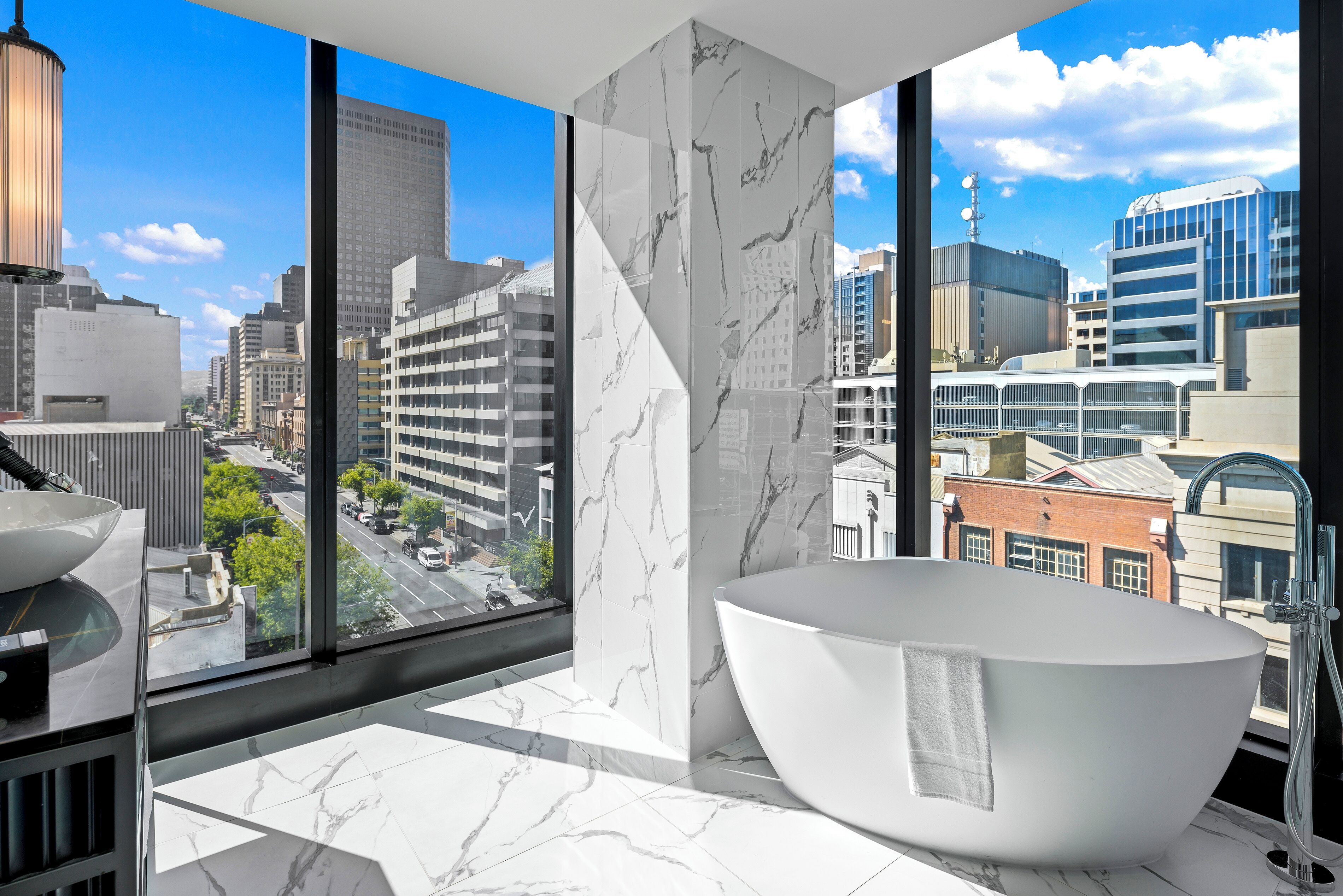 Un baño moderno con una bañera grande, paredes de mármol y vistas a la ciudad.