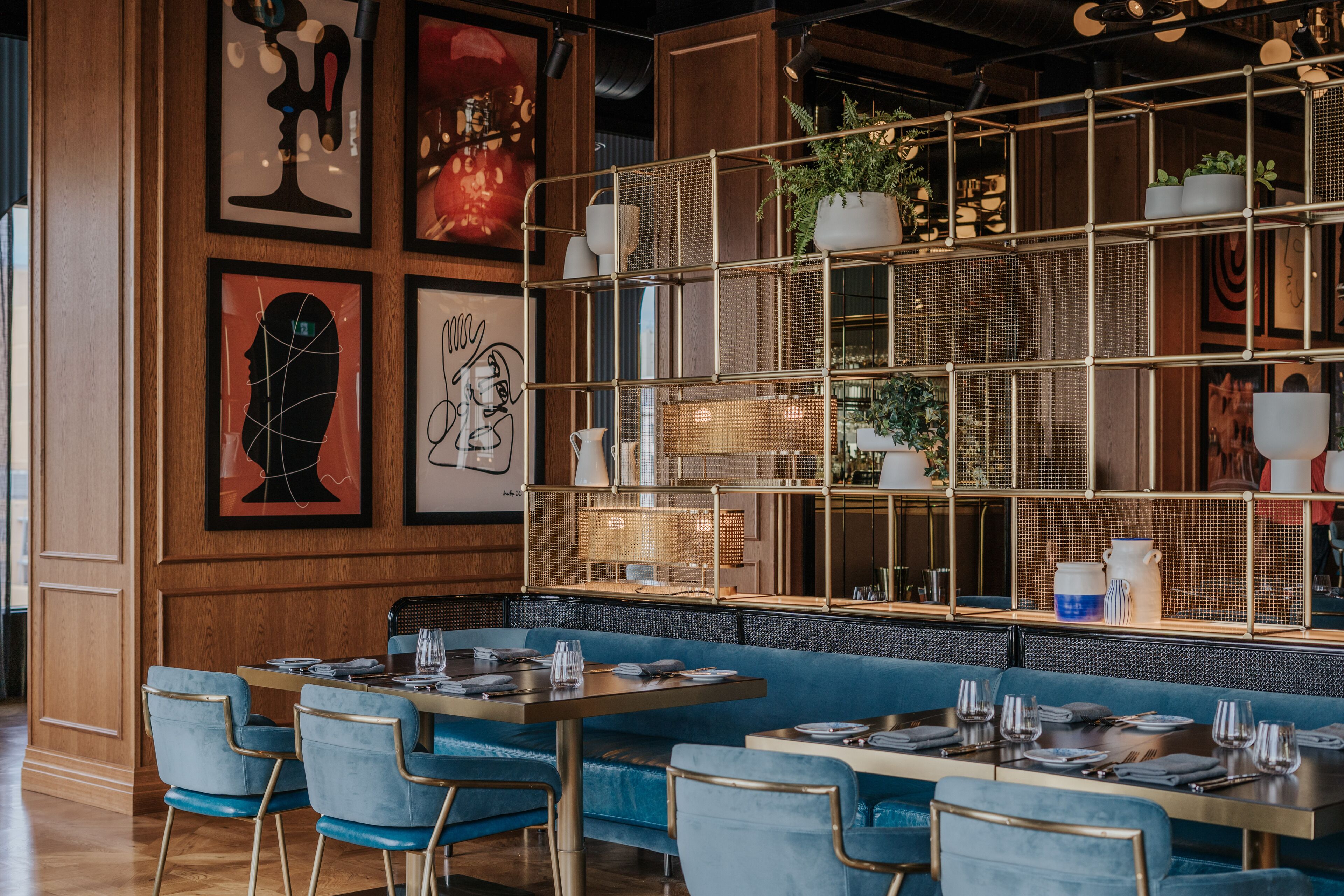 Un restaurant avec des chaises et des tables recouvertes d’un tissu bleu, des lambris en bois sur les murs et des œuvres d’art encadrées.