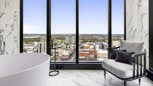 Un bagno moderno con una vasca da bagno ampia, una poltrona e vista sulla città attraverso ampie finestre.