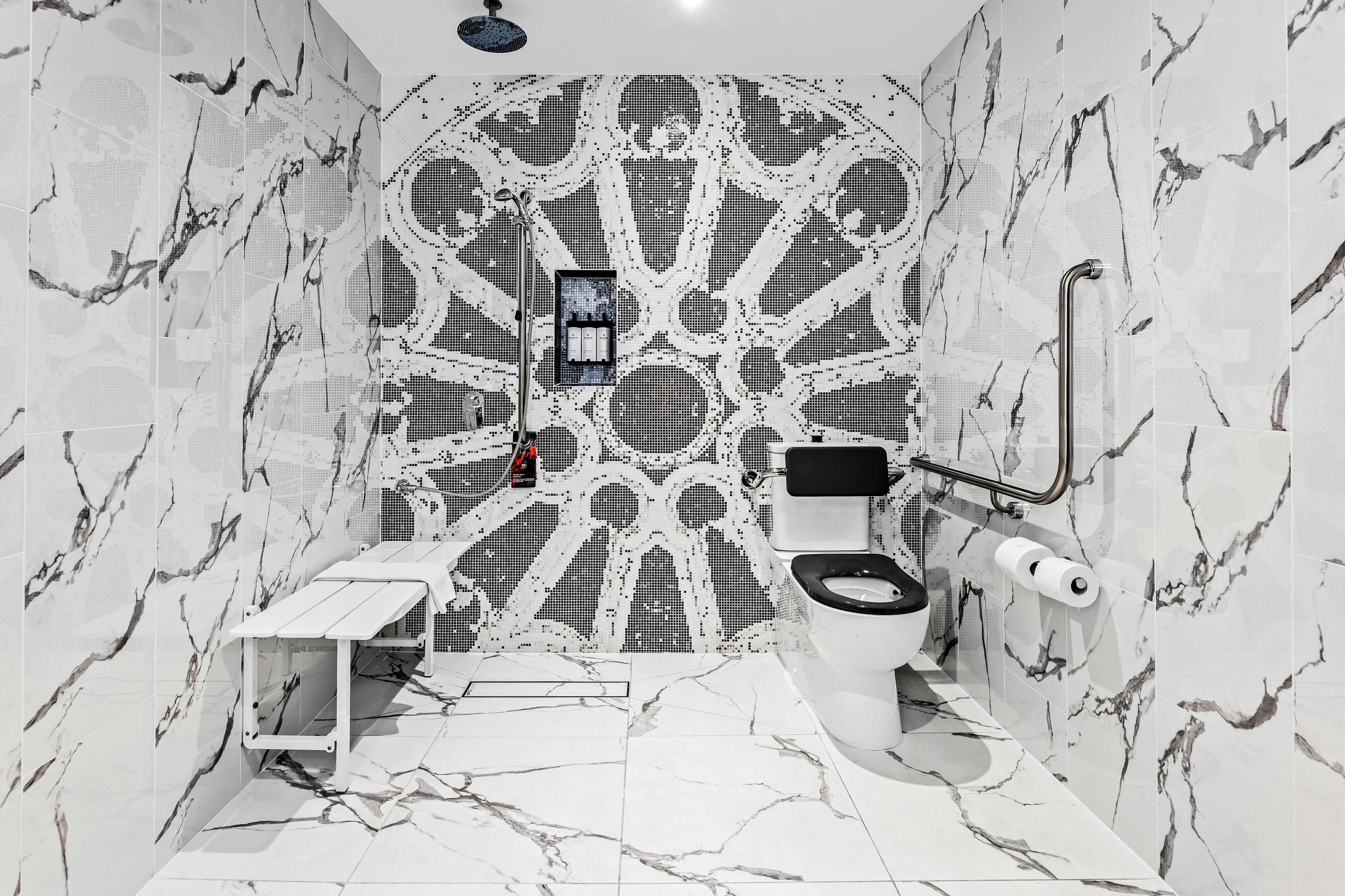 A bathroom with a unique geometric tile design, a modern toilet, and a handheld showerhead.