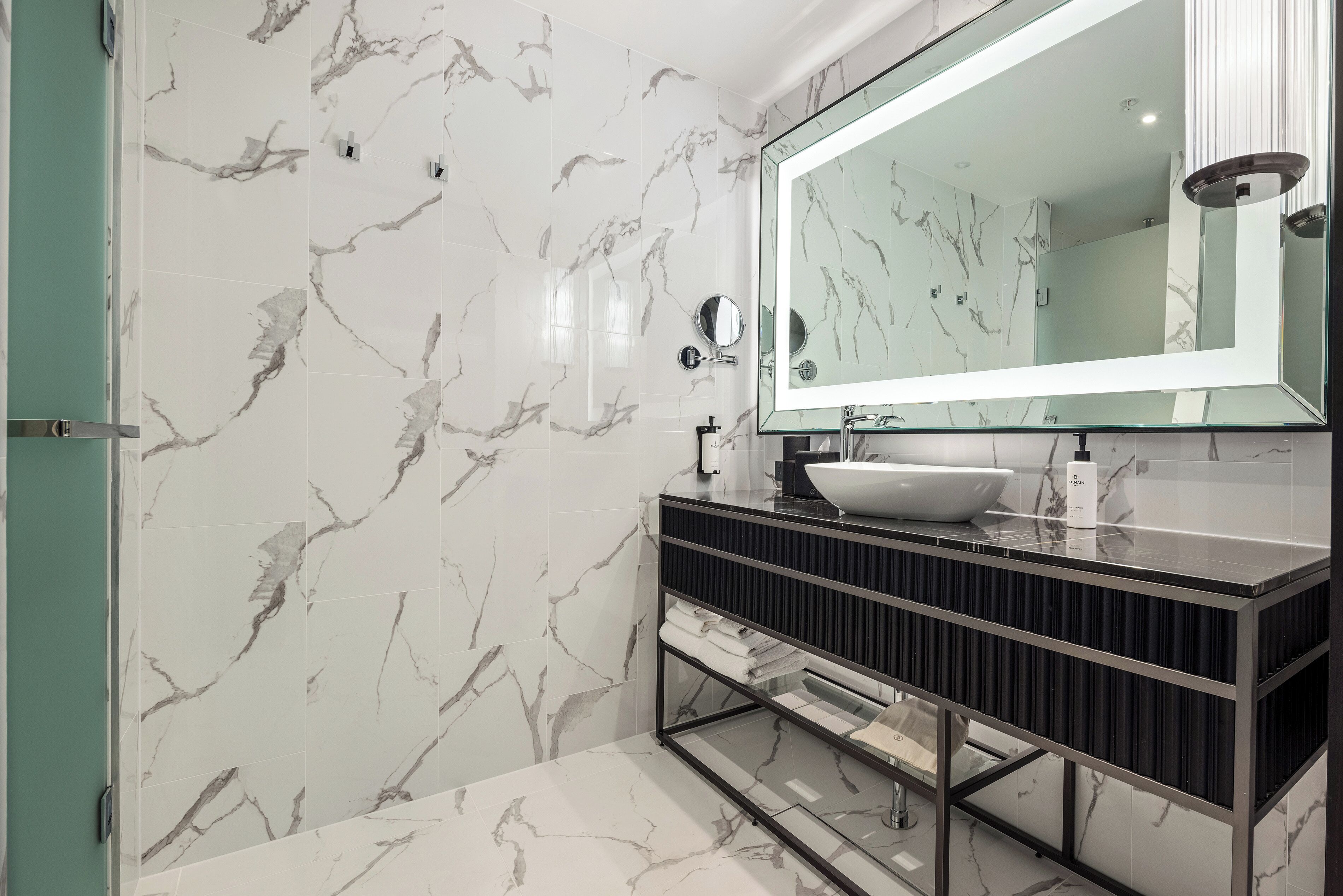 A bathroom with a marble wall, a large mirror, a black vanity, and a white sink.