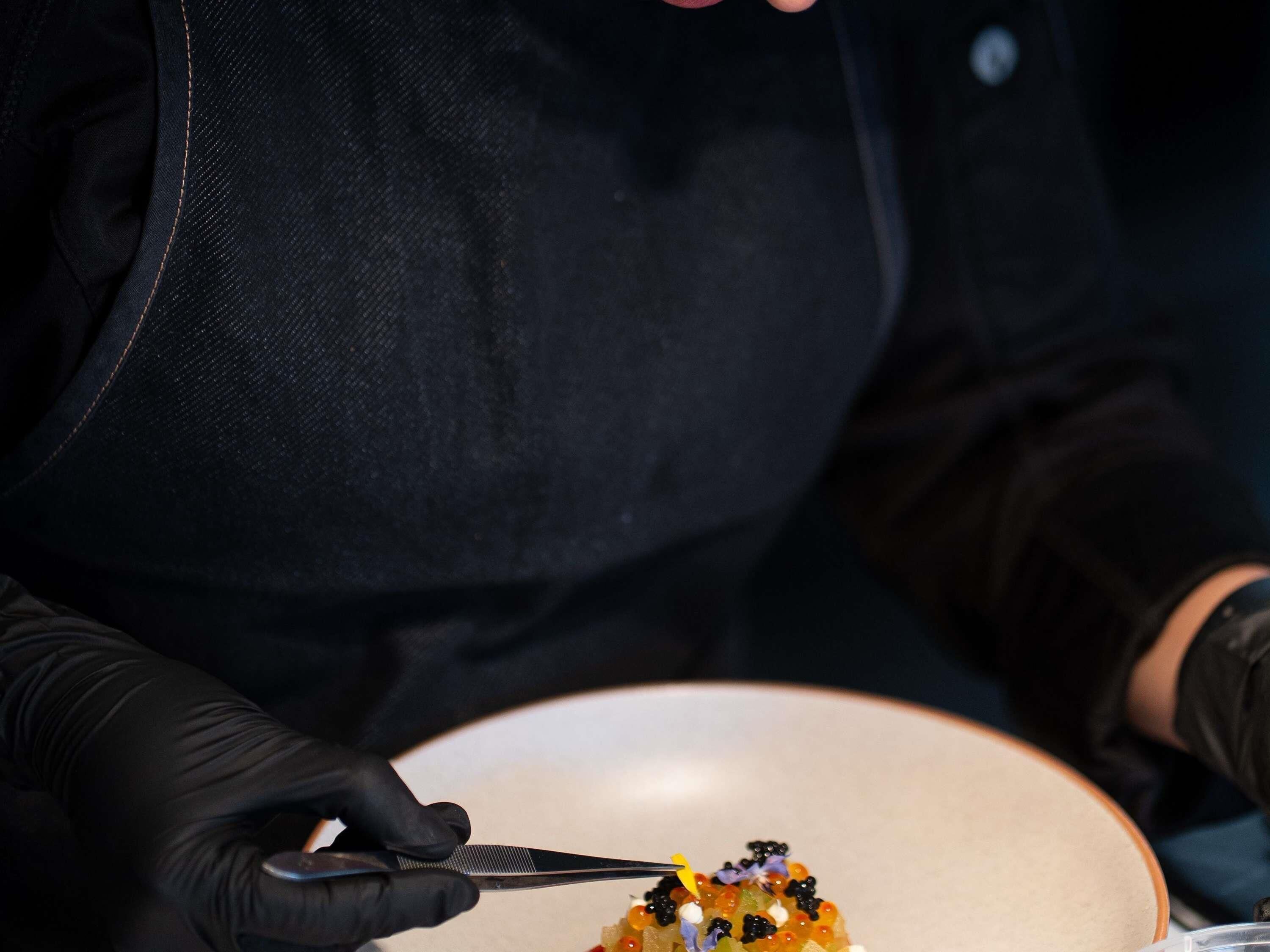 Una persona con guantes negros sirve un plato con diversos alimentos.