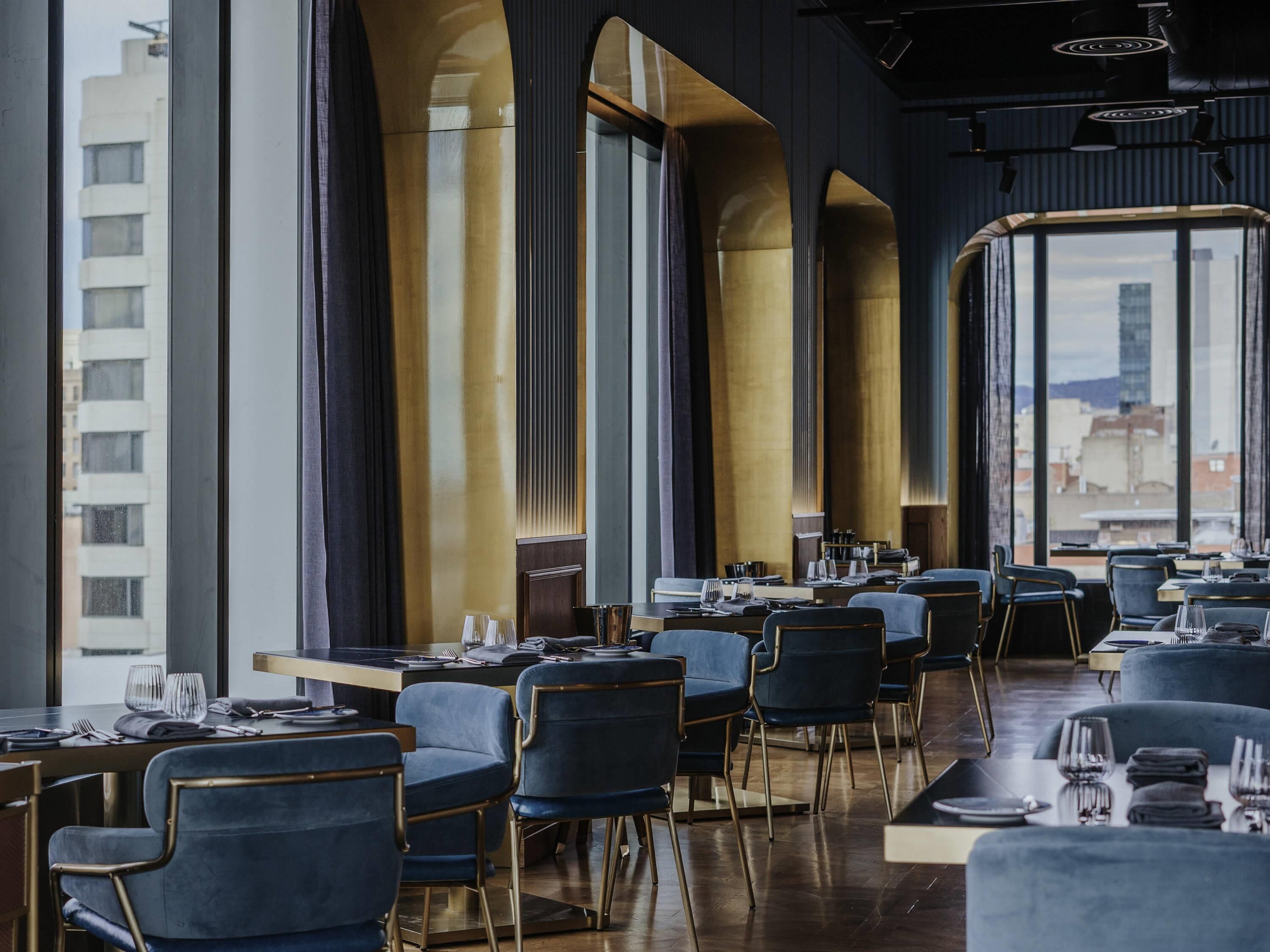 Ein modernes Restaurant mit hohen Decken, großen Fenstern und Blick auf die Stadt.