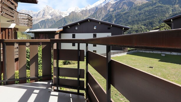 A balcony with a view of snow-capped mountains and a modern building in the background.