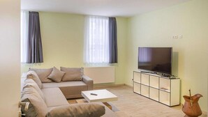 A modern living room with a sofa, a coffee table, a TV on a stand, and a decorative vase. - Ferienwohnung Fachwerktraum, Wernigerode (Wernigerode)