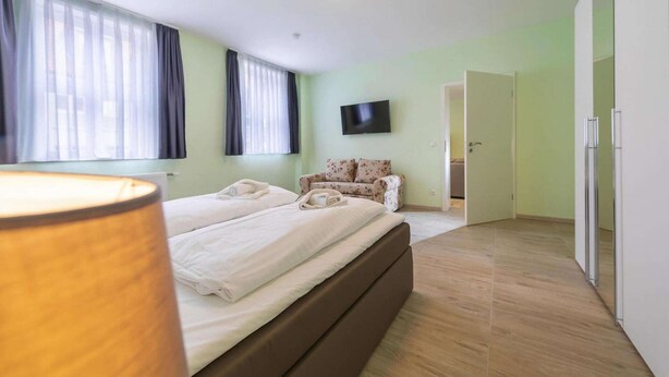 A bedroom with a bed, a TV, a sofa, and a door leading to another room. - Ferienwohnung Fachwerktraum, Wernigerode (Wernigerode)