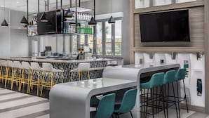 Zona de bar moderna con mostrador, asientos y una amplia pantalla de televisión.