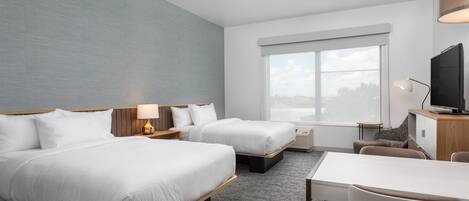 A hotel room with two beds, a desk, a chair, a television, and a large window.