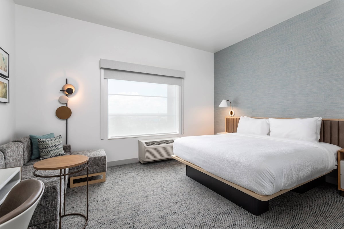 Una habitación de hotel moderna con una cama grande, una mesita redonda pequeña, un sofá y una lámpara fijada a la pared.