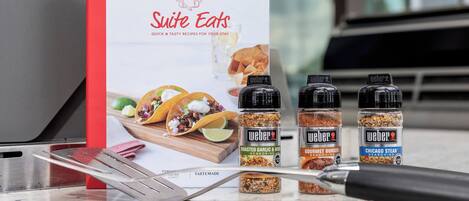 Un libro de cocina titulado 'Suite Eats' con imágenes de tacos y un set de condimentos Weber sobre una encimera de cocina.